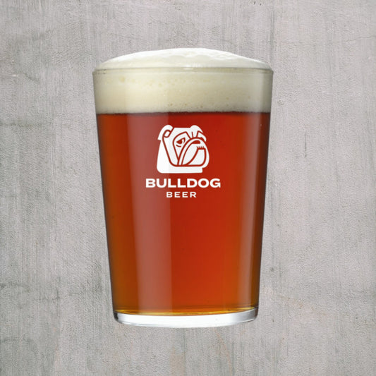 Glas med Bulldog logo fyllt med öl med skum på toppen mot grå bakgrund