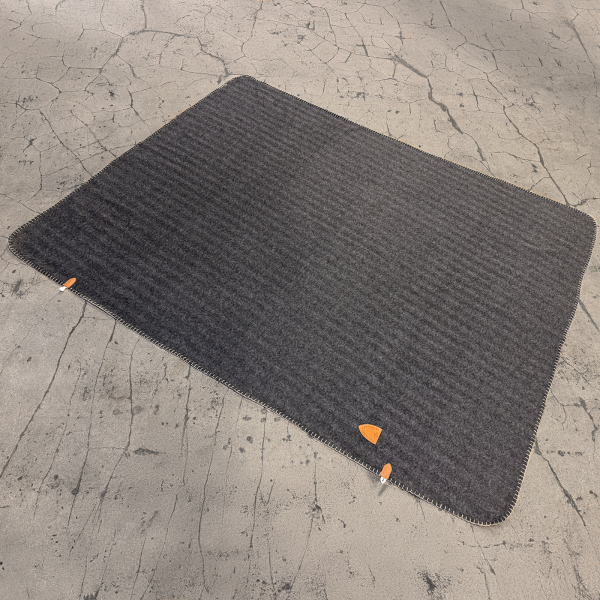 Grå pläd med brunt konstläder märke med logotyp. mot stenfärgad bakgrund