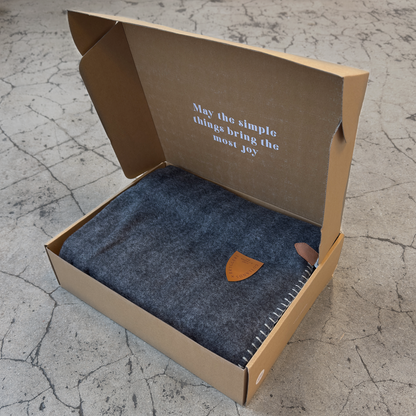 Brun öppen kartong med grå pläd inuti. mot stenfärgad bakgrund