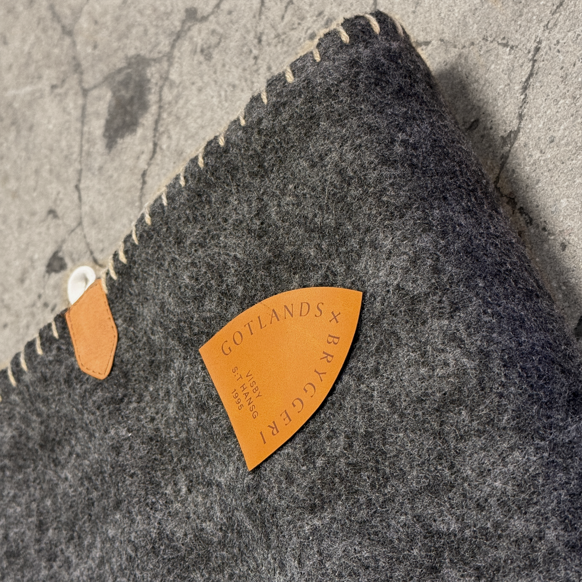 Grå pläd med brunt konstläder märke med logotyp i närbild. mot stenfärgad bakgrund