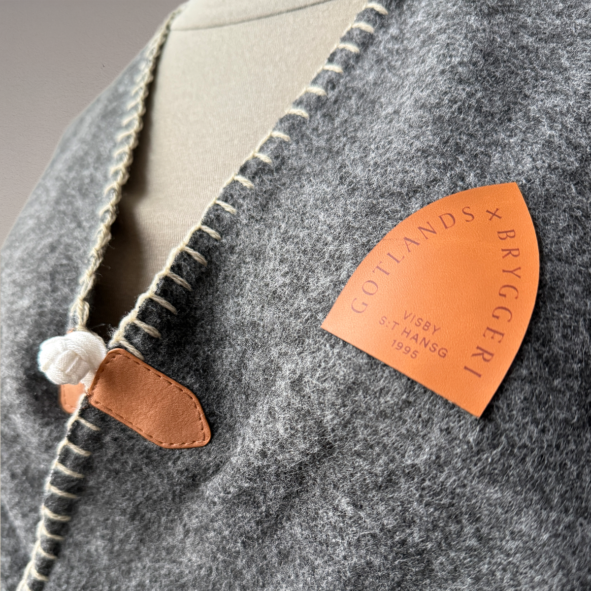 Grå pläd med brunt konstläder märke med logotyp  i närbild.