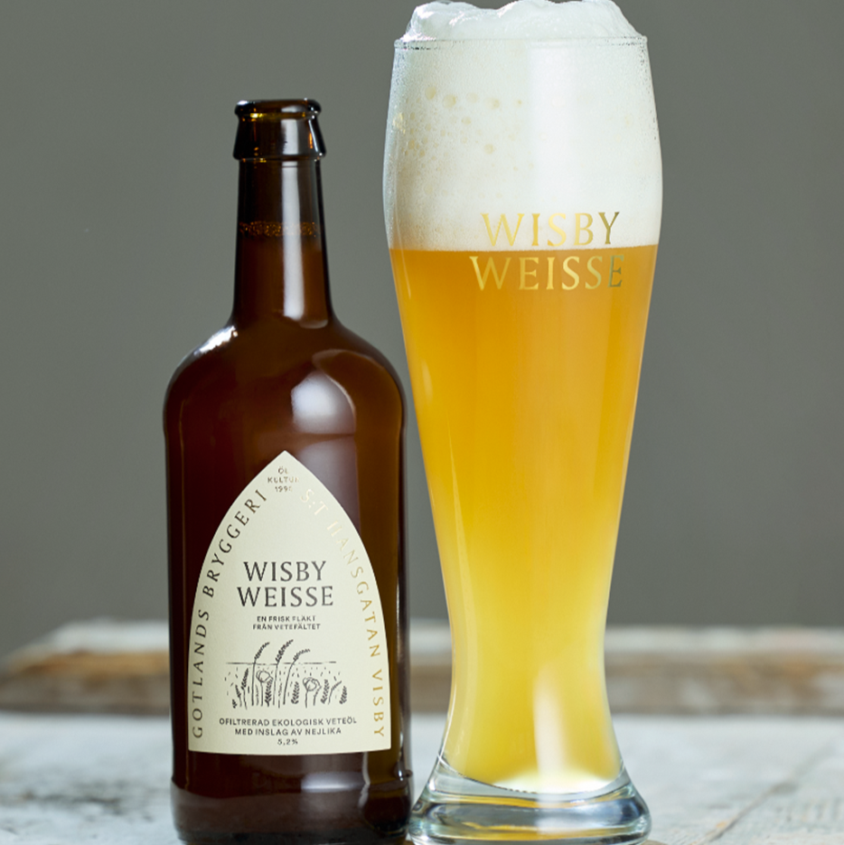 glas med wisby weisse logo med öl i skum på toppen bredvid en flaska Wisby Weisse